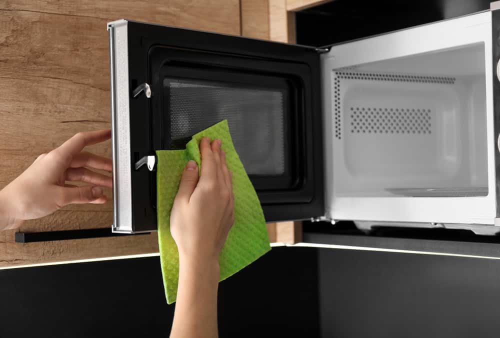 Woman cleaning microwave oven with rag in kitchen
