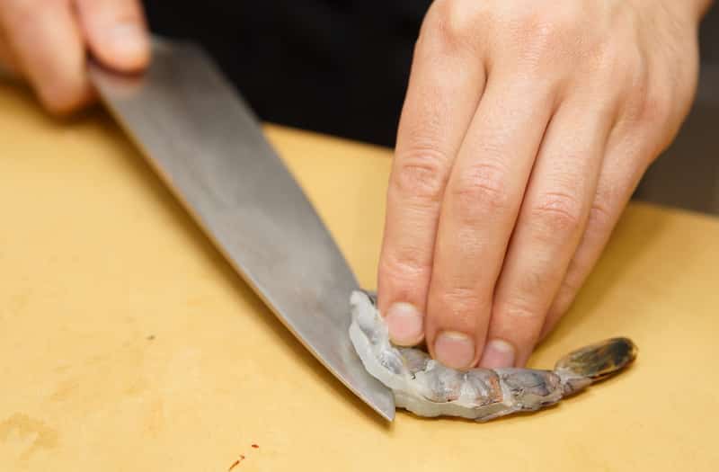 Chef is cutting raw shrimp on plastic plank