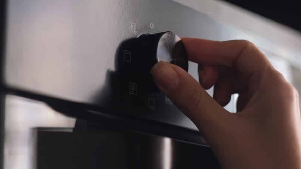 Close up of woman hand turning round temperature oven handle in the kitchen at home