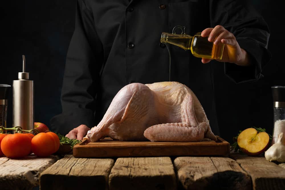 The chef pours olive oil over a whole carcass of chicken turkey