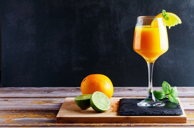 Glass of orange and lime juice with mint on wooden table