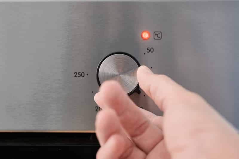 A man's hand turning an oven thermostat