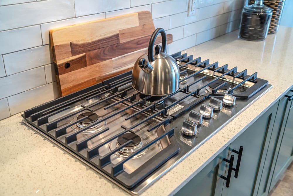 Kettle over five burner cooktop built into the kitchen countertop with cabinets