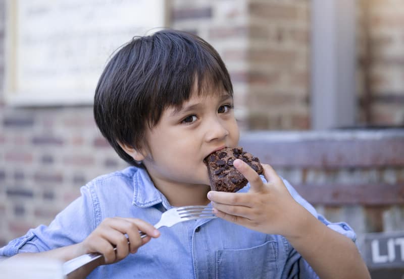 Little boy enjoy eating chocolate cake in outdoors cafe