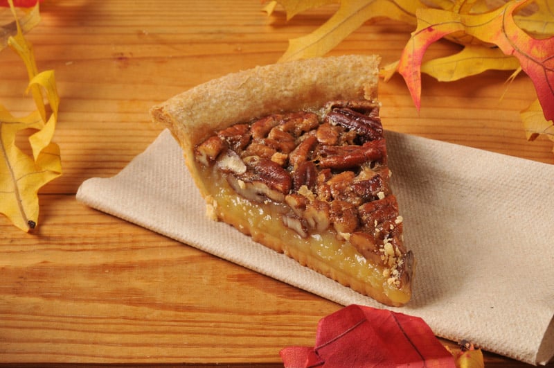 A slice of pecan pie with autumn leaves on a rustic wooden counter