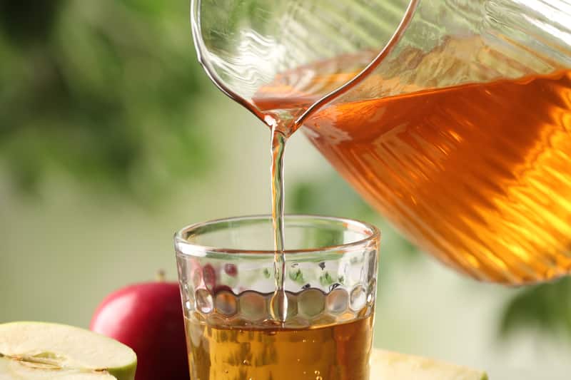Pouring apple juice into glass on blurred green background