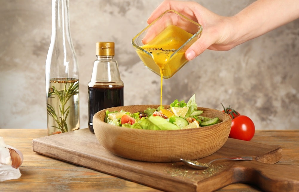 pouring honey mustard dressing into bowl with fresh salad