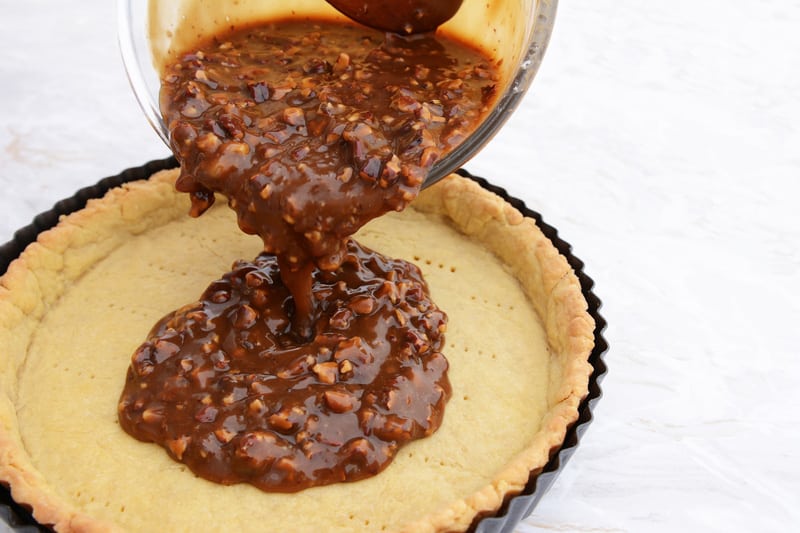 Pouring pecan pie filling into a pastry case