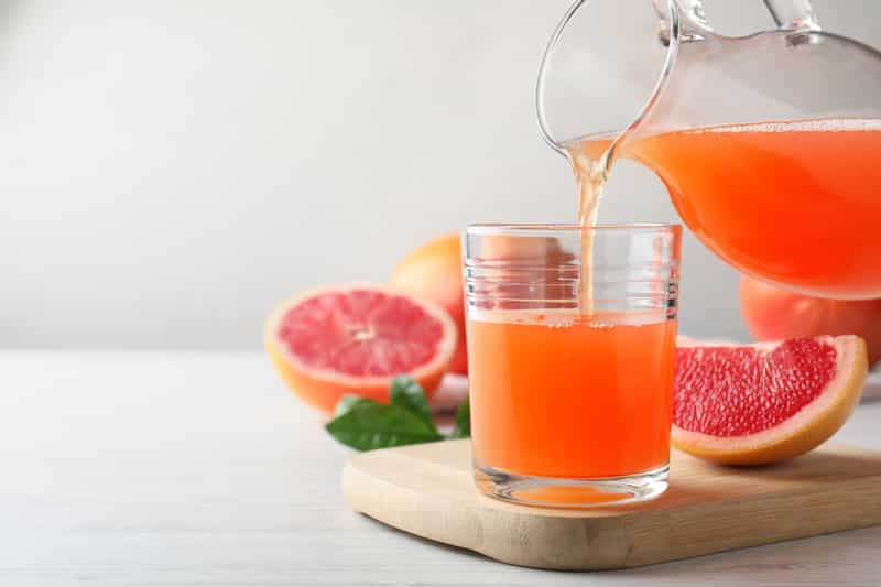 Pouring tasty freshly made grapefruit juice into glass on white wooden table