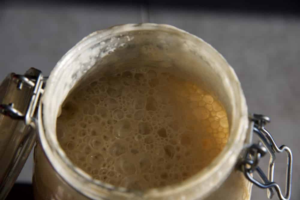 Sourdough starter rising and bubbling in a clear glass storage jar