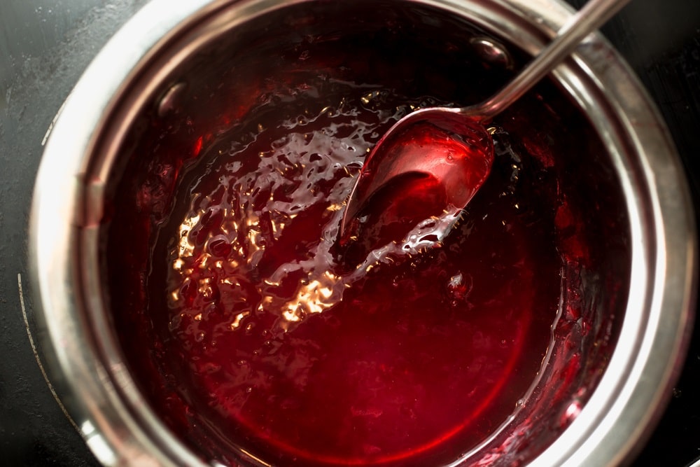 stirring cherry jam with spoon in metal saucepan