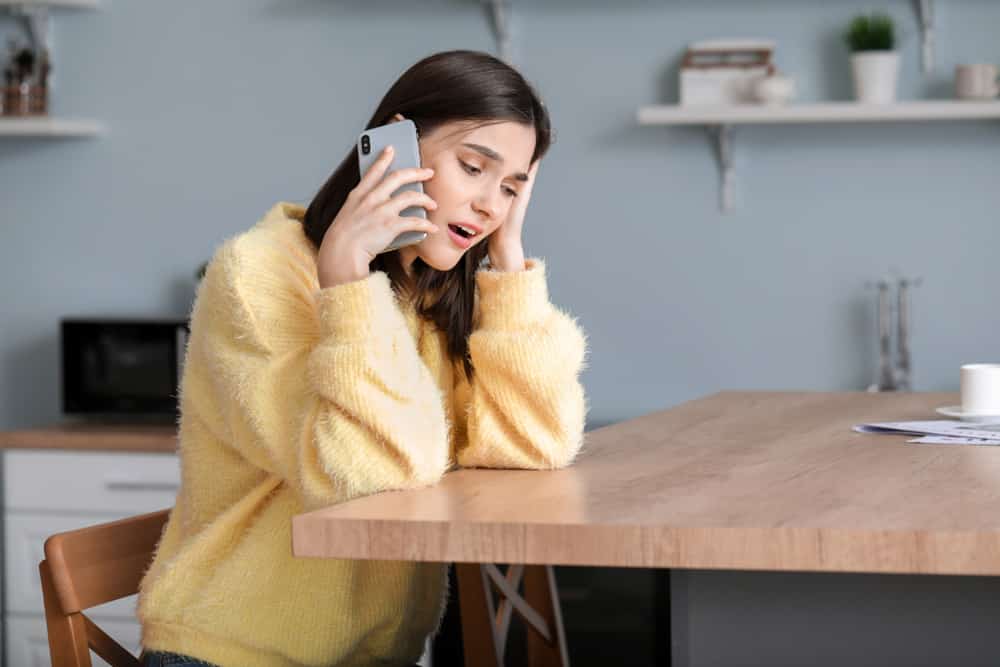 Worried young woman talking by phone at home