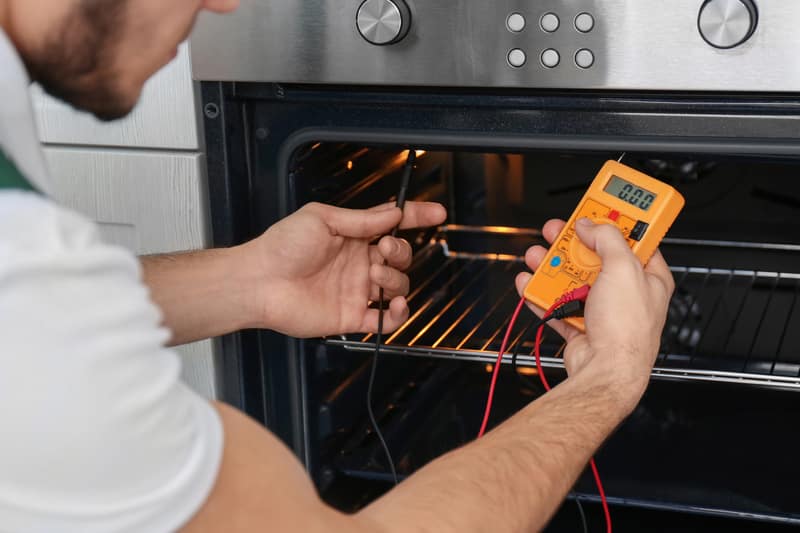 Young man with multimeter repairing oven