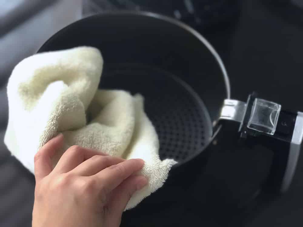 Women’s hand wipe the air fryer basket with kitchen towel