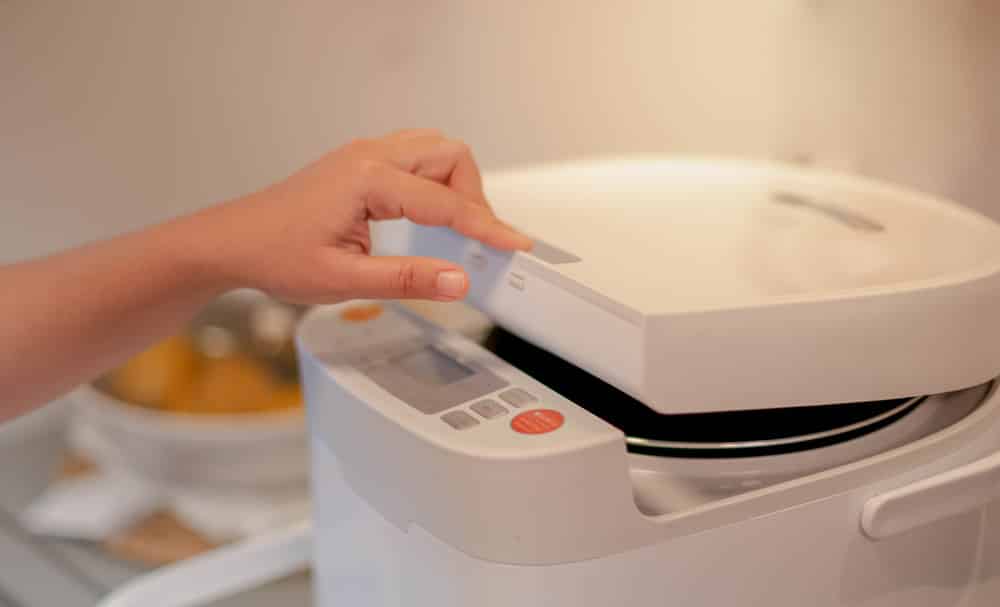 Female hand pushing on the button of the new modern rice cooker