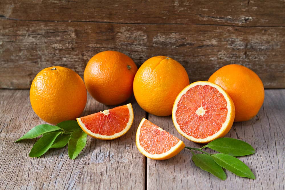Fresh oranges with slices and leaves on wooden background