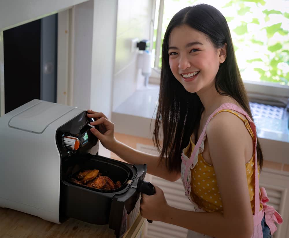 Asian girl cooking a fried chicken by Air Fryer machine in her kitchen at home