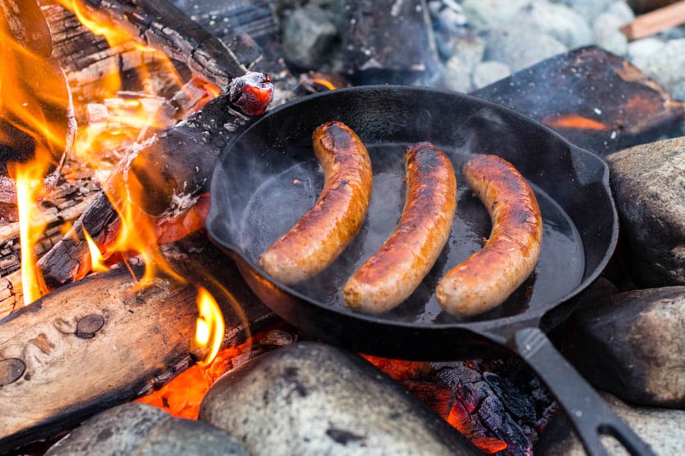 Live fire cooking juicy sausages over campfire