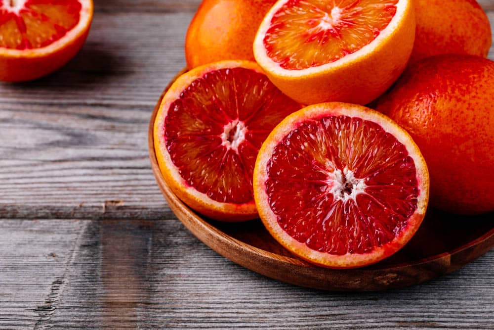 Sliced and whole ripe juicy Sicilian Blood oranges on wooden background