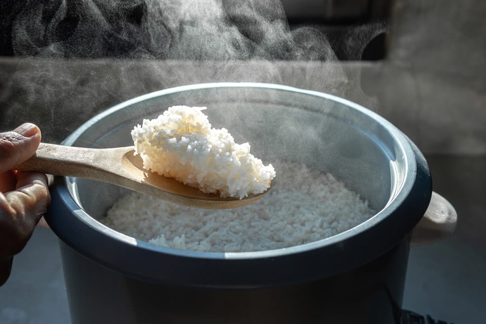 The steam from Hand hold wooden ladle in electric rice cooker in the kitchen