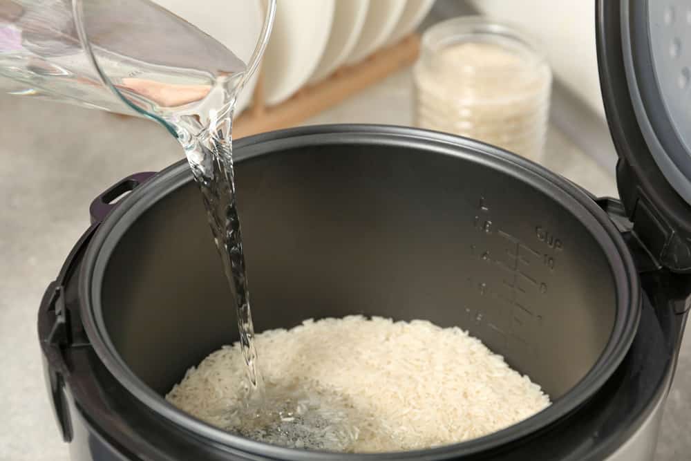 Water pouring into modern rice cooker in kitchen