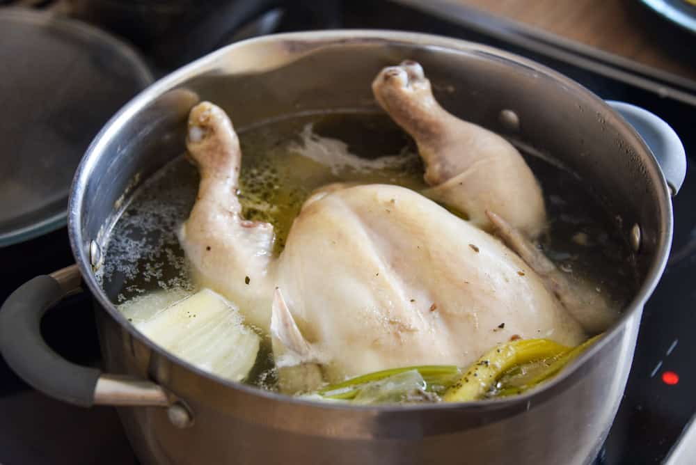 whole chicken in soup cooking in a pan on the stove