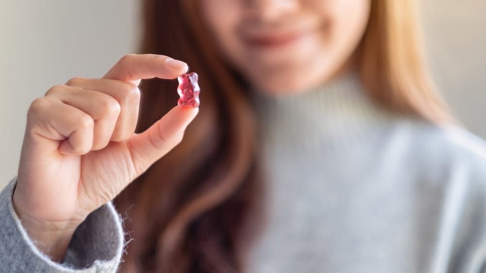 Closeup image of a woman holding and looking at a red jelly gummy bear