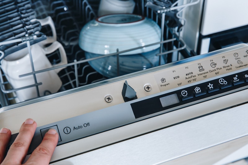 Close-up of woman's finger pressing start button on dishwasher in the kitchen