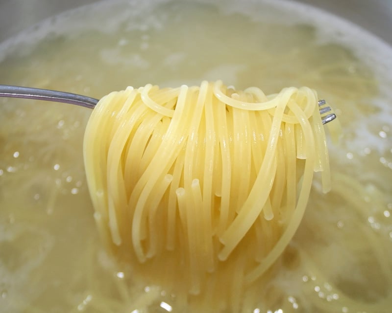 Cooked pasta noodles being lifted out of pot of boiling water with fork