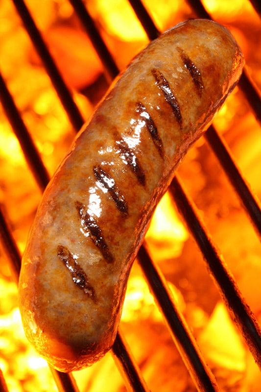 Cooking a sausage hot dog on barbecue grill