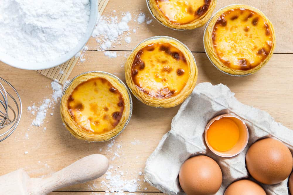 Egg tarts, eggs and other ingredients and tools on table
