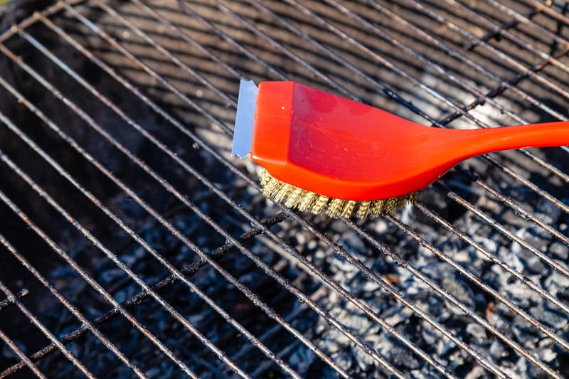 Close-up of a red brush with golden bristles and a scraper for cleaning a barbecue grill grate