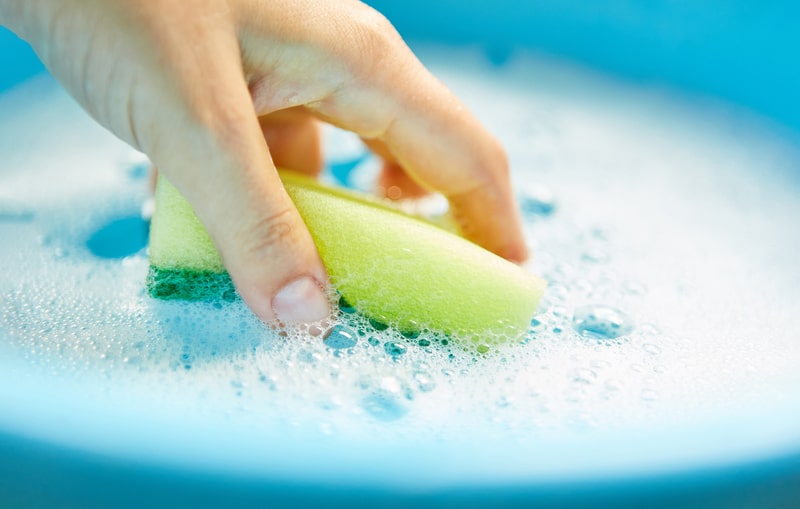 Hand dips sponge in soapy water while cleaning house