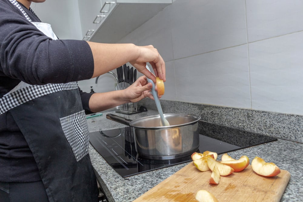 Hands cooking caramelized apples in a pot on an induction cooker