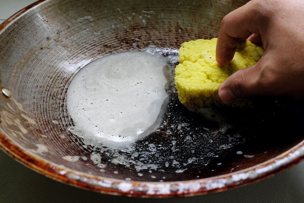 Human hand scrubbing or cleaning a burnt, scorched and greasy pan