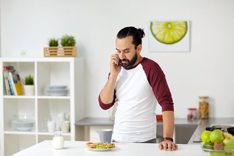 Man calling on smartphone and eating at home