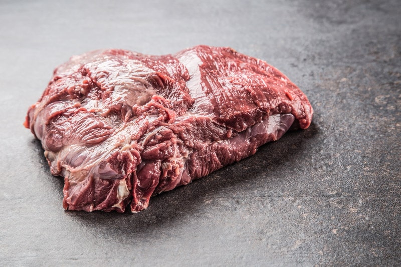 Portion of raw beef neck on dark butcher board