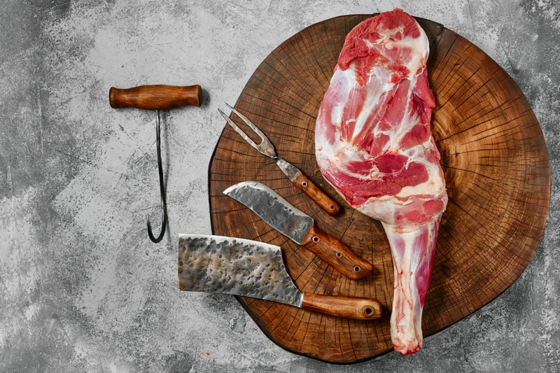 Raw lamb shoulder on butcher`s cutting log with tools
