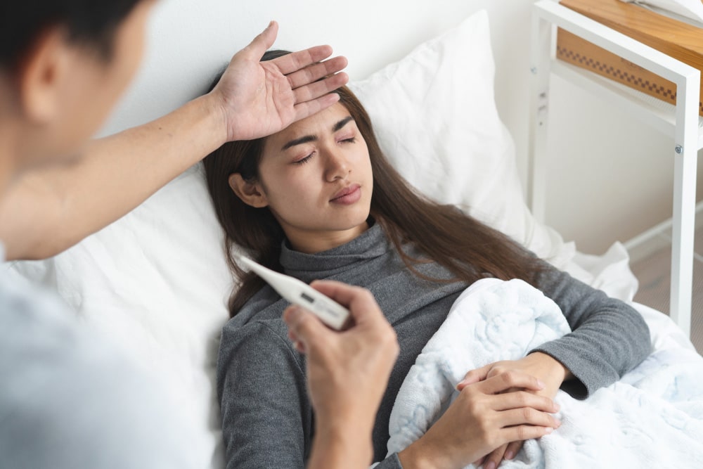 Young Asian woman lying on the bed have a fever and her husband checking thermometer and measure body temperature