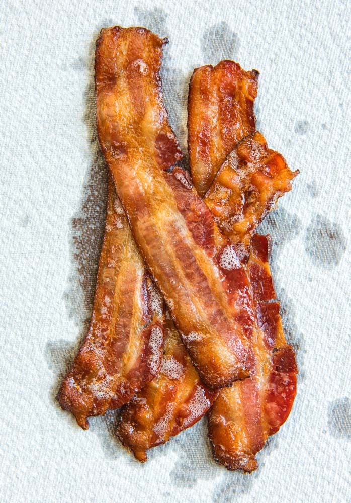 Strips of cooked bacon piled up on a white paper towel