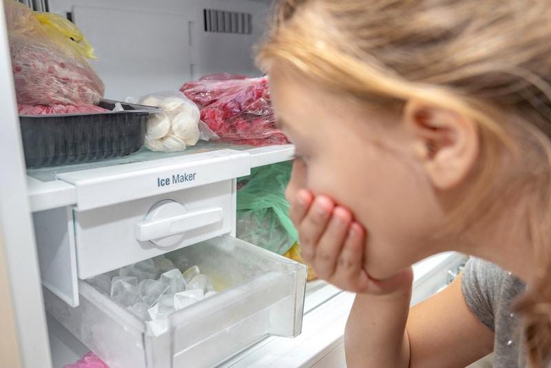 A surprised girl looks at the full ice cube tray of the freezer ice maker