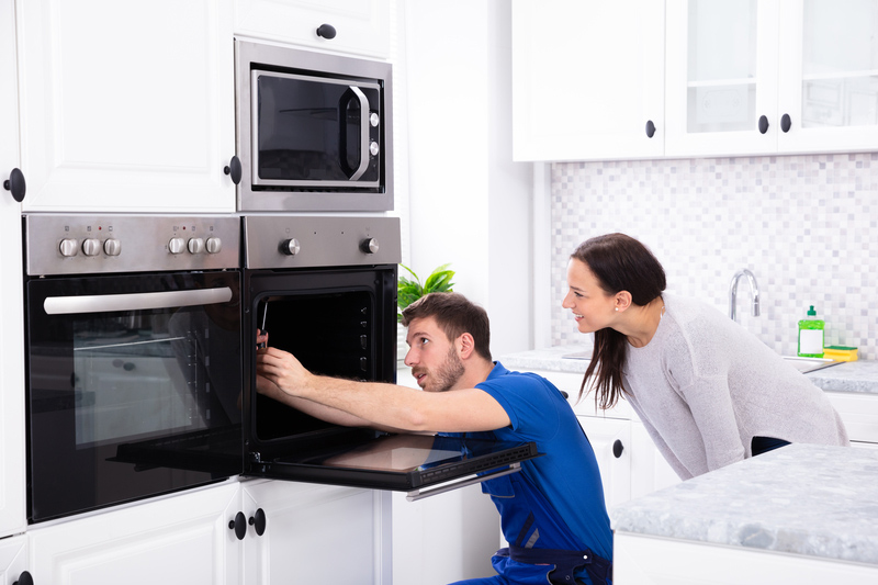 Technician In Overall Fixing Oven In Kitchen