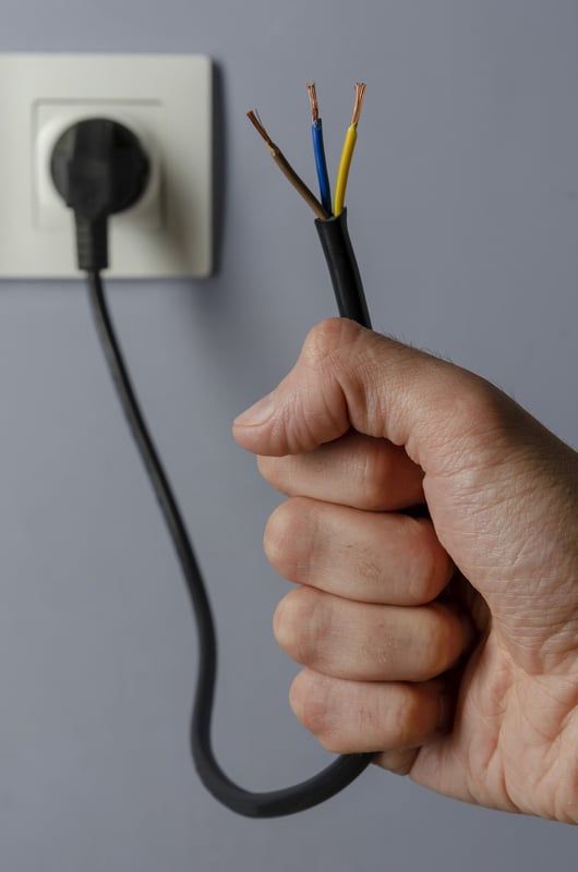 a hand holds an electrical cable plugged into an outlet