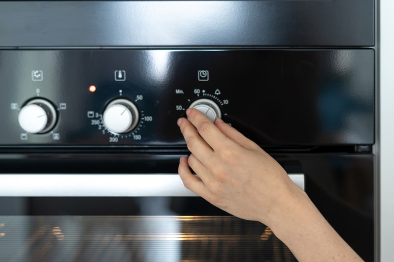 Woman hand turning switch at modern built in oven and select program