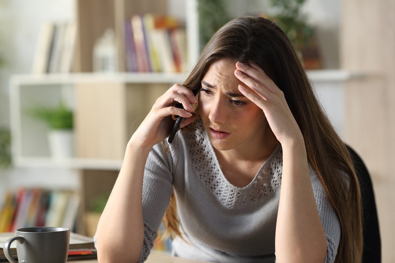 Worried woman calling on phone sitting at home