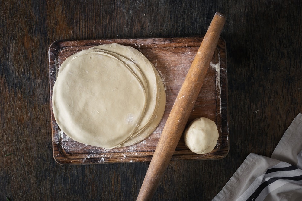 Raw fresh dough on a wooden board with rolling pin