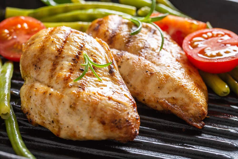 Barbecued chicken breasts on a grill pan with fresh green vegetable and chery tomatoes and rosemary twigs