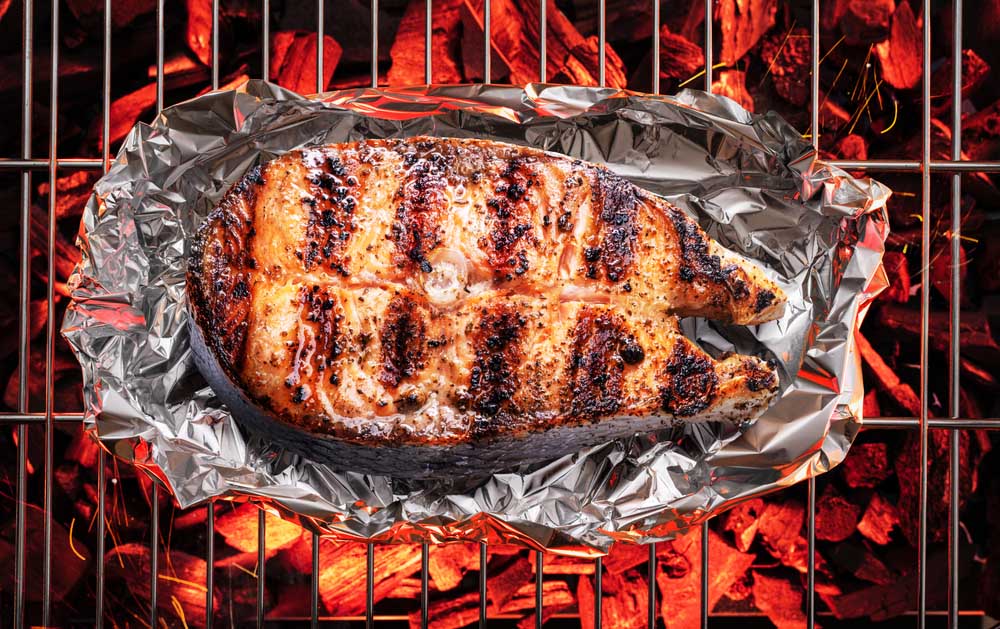 Grilled salmon steak on BBQ grate over hot pieces of coals