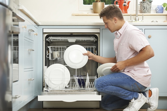 Man Loading Dishwasher In Kitchen