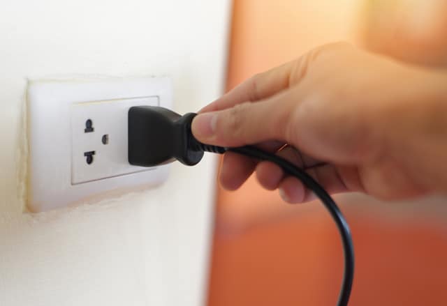 Plug in wall with hand and black power cord cable